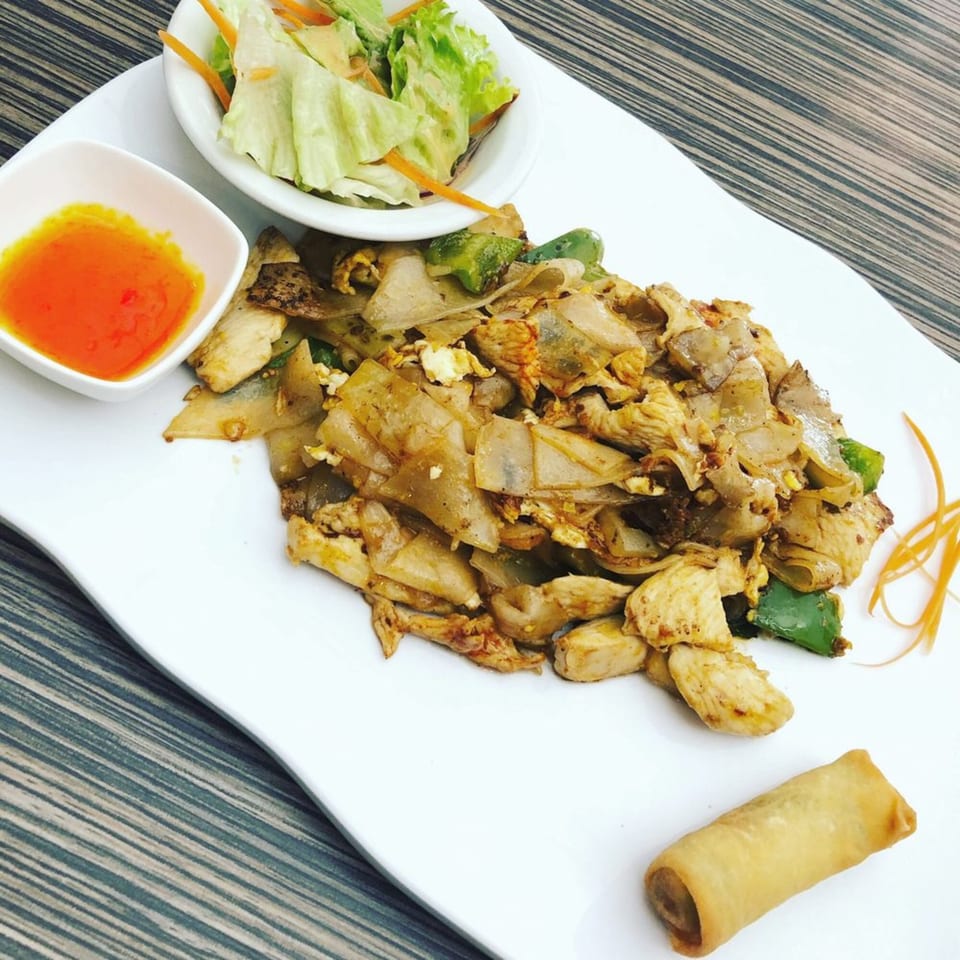 Kanda Thai Cuisine's Pad See Ew with chicken, a side salad, sweet chili sauce, and an egg roll.