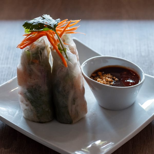 Two fresh spring rolls with shredded carrots and cilantro, served with a side of peanut sauce.