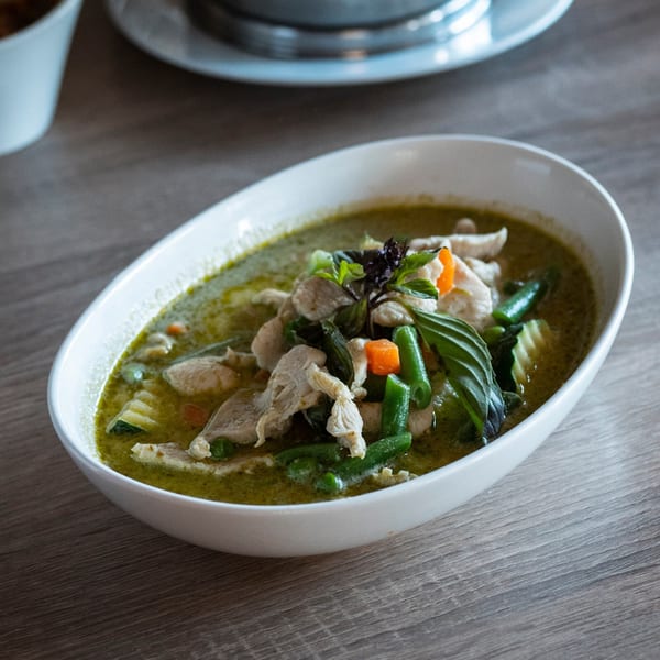 A white oval bowl filled with Kanda Thai Cuisine's green curry, chicken, and vegetables.