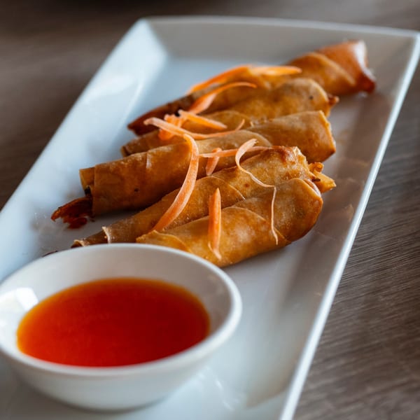 Crispy Thai spring rolls with shredded carrots and a side of sweet chili dipping sauce.